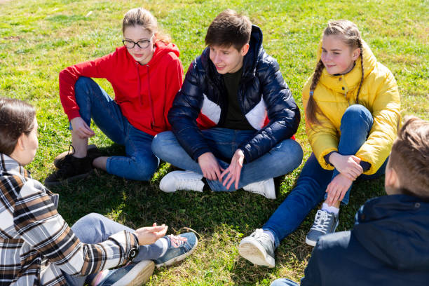 istock Cheerful teens sitting on green lawn and talking 1239350184