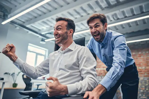 Young smiling male partners having fun in modern office next to workstation