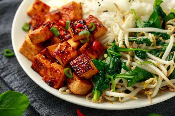 Fried Asian tofu in sweet chilli glaze served with rice, steamed spinach and beansprouts. Vegetable healthy food.