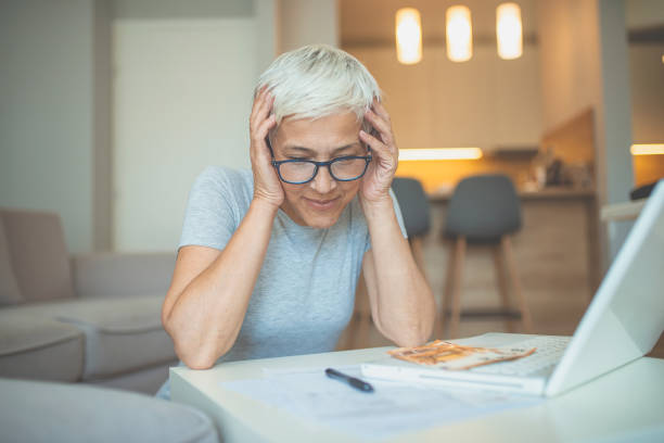 istock Old freelancer writing details on book while working on laptop in living room 1239466124