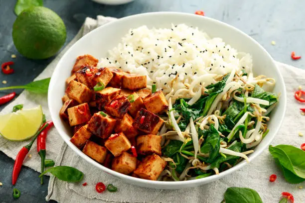 Fried tofu in sweet chilli glaze served with rice, steamed spinach and beansprouts in white bowl. Vegetable healthy food.