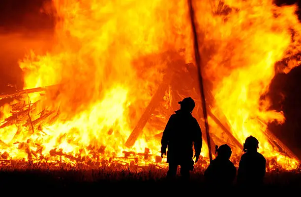 Three firefighters outlined against a massive blaze