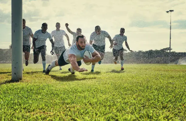 Full length shot of a handsome young rugby player scoring a try while training on a rainy day