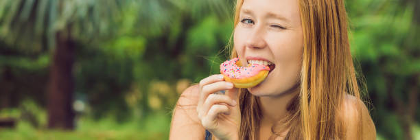 portrait of a young woman eating a donut against a plant background BANNER, long format portrait of a young woman eating a donut against a plant background. BANNER, long format big fat lips stock pictures, royalty-free photos & images
