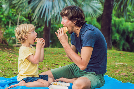 Portrait of a young father and his son enjoying a hamburger in a park and smiling.