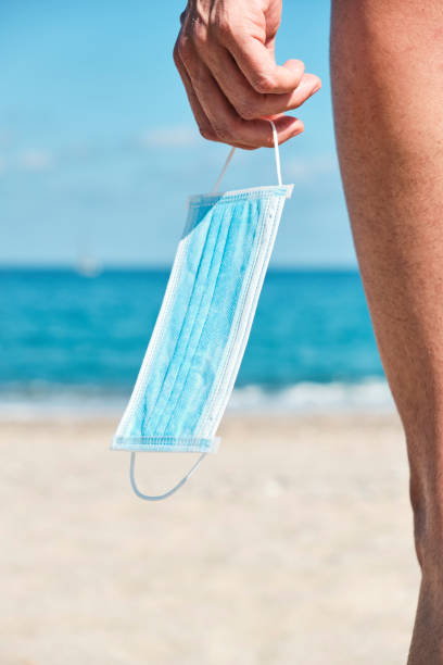 istock man with a surgical mask in his hand on the beach 1239489843