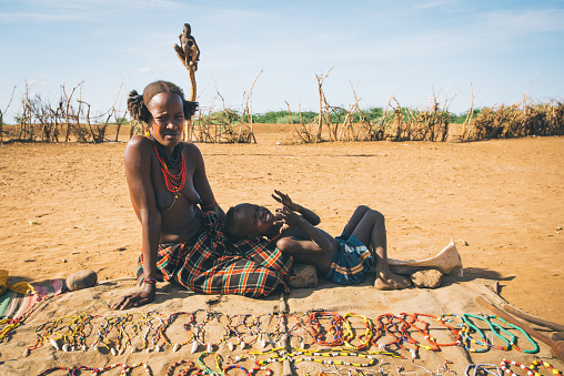 Omorate, Omo Valley, Ethiopia - May 11, 2019: Woman from the African tribe Dasanesh with baby offering handmade souvenirs. Daasanach are Cushitic ethnic group inhabiting in Ethiopia, Kenya, and South Sudan