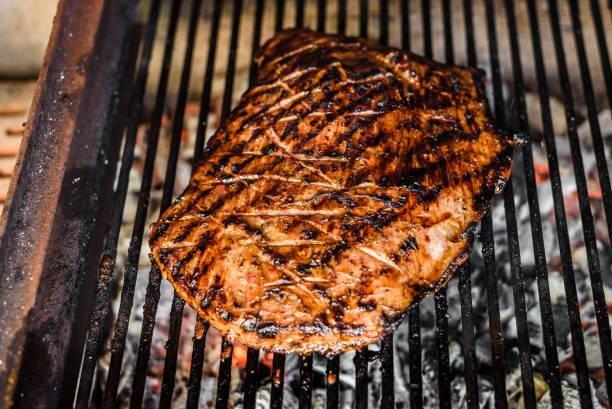 istock Grilling marinated angus beef flank steak on hot coals barbecue grill. 1239491996