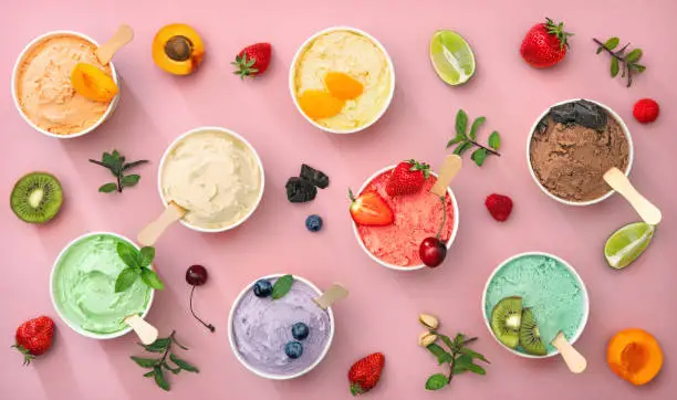 Various colorful ice cream sorts with fruits in paper cups on pink background