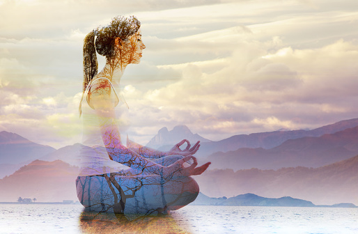 Silhouette of woman doing yoga in lotus position over lake landscape. Concept of connection with the universe and nature.