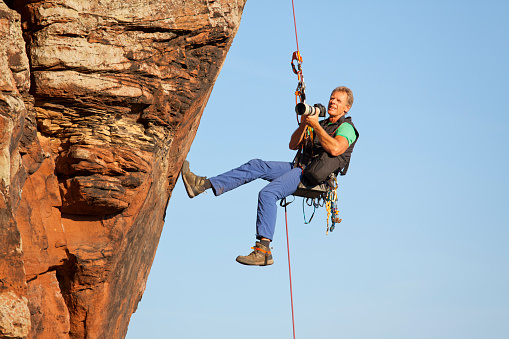 Photographer and rock climber Norbert Frank taking pictures while hanging in front of a rock