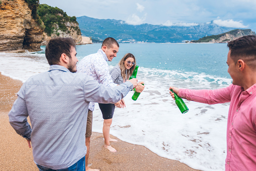 Five caucasian young people having small beer party on beach.