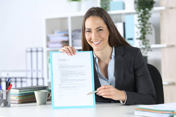 happy executive points contract looking camera at office - endorsing business application form filling imagens e fotografias de stock