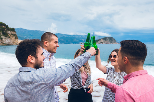 Five caucasian young people having small beer party on beach.