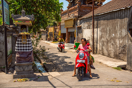 Bali, Indonesia - December 01, 2019: Traditional Balinese Tribe Village. Scooter drivers wait on crossroads. Scooter is a popular balinese transport