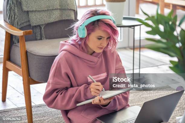Focused Hipster Teen Girl School College Student Pink Hair Wear Headphones Write Notes Watching Webinar Online Video Conference Calling On Laptop Computer Sit On Floor Working Learning Online At Home Stock Photo - Download Image Now