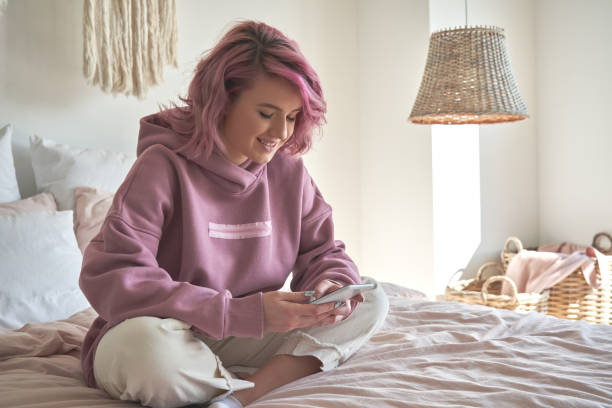 улыбающаяся хипстерская девушка-подросток с розовыми волосами держит смартфон в чате в социальных сетях, смотрит видеоконтент, текстовые � - gen z стоковые фото и изображения
