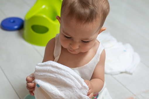 The concept of learning to use the chamber pot. close-up: a little cute baby holds clean diapers in his hands and looks at them. in the background a pot in blur