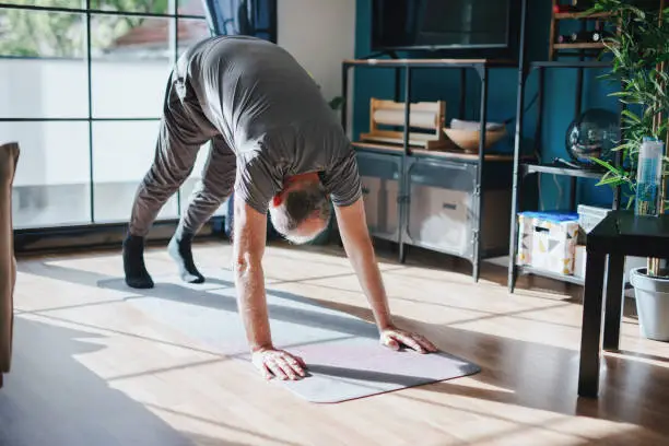 Photo of Senior man doing Downward-facing dog, watching youtube videos and learning the exercises