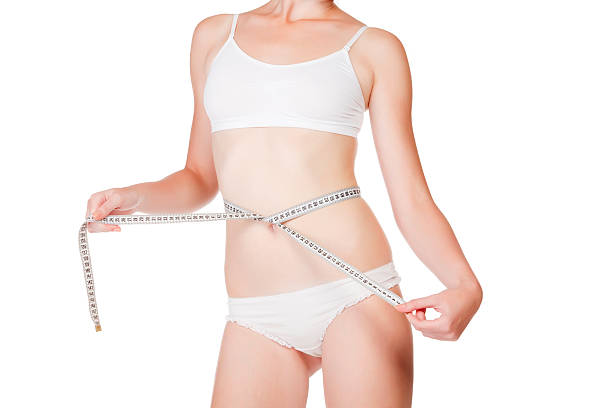 Woman measuring size of her waist Woman measuring size of her waist with a tape measure. Isolated on white background exercising tape measure women healthy lifestyle stock pictures, royalty-free photos & images