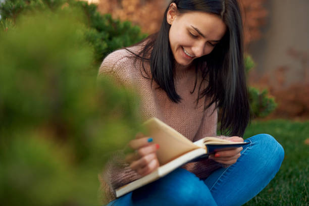 istock Smiling young female is reading book outdoors 1239593268