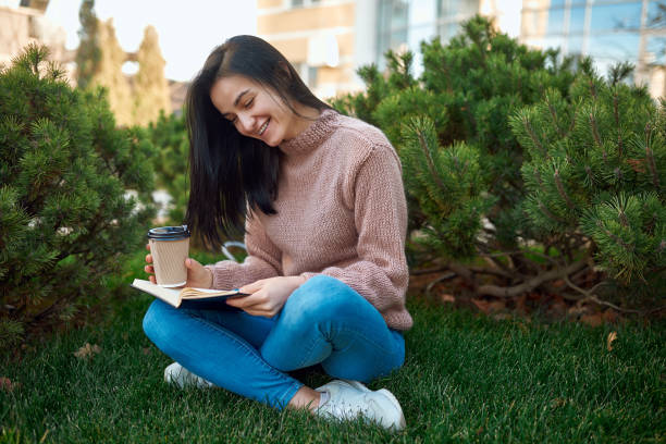istock Pretty female smiling while reading interesting book outdoors 1239593303