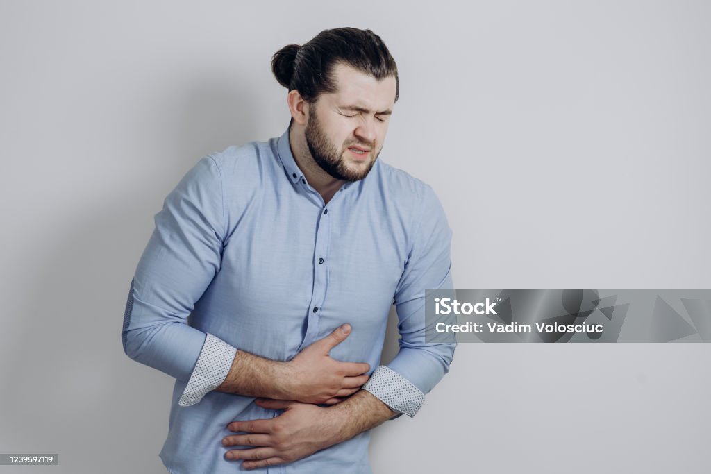 A guy with curly hair clings to his stomach. Discomfort of a health problem A guy with curly hair clings to his stomach. Discomfort of a health problem. High quality photo Abdomen Stock Photo