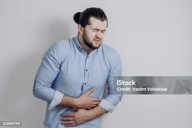 A Guy With Curly Hair Clings To His Stomach Discomfort Of A Health Problem Stock Photo - Download Image Now