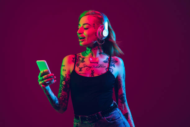 porträt der jungen kaukasischen frau auf lila hintergrund mit copyspace, ungewöhnliche und freaky aussehen - headphones music mobile phone tattoo stock-fotos und bilder