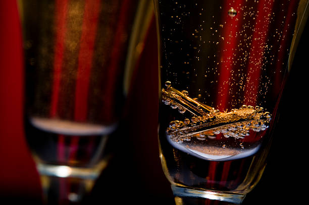 Close-up of a pair of wedding rings in a champagne flute against a red curtain background