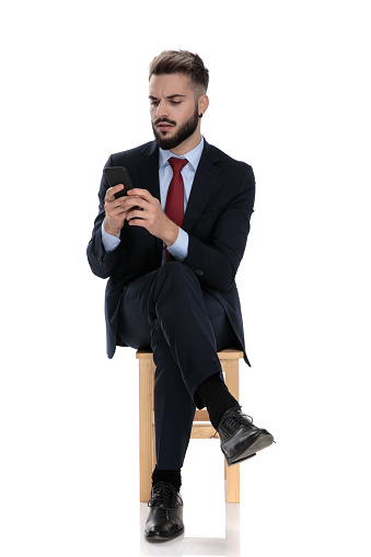 concerned young businessman checking emails and texting messages on cellphone, sitting isolated on white background