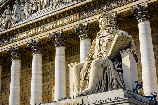 Low angle view of the statue of Francois d'Aguesseau in front of the neoclassical facade of the Palais Bourbon, seat of the french National Assembly in Paris, France.