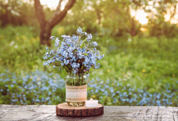 Bouquet of wild flowers Myosotis also known as Forget me not s or scorpion grasses in lace burlap cloth decorated baby food jar. Inexpensive vintage party decorations concept. Cozy spring evening. ramo de flores silvestres myosotis también conocido como forget me no s o hierbas de escorpión en tela de arpillera de encaje decorado frasco de comida para bebés. concepto de decoraciones vintage de fiesta de bajo costo. acogedora noche de primavera.