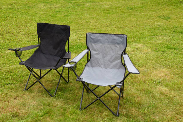 Two empty folding camping chairs in grass Two grey and black empty folding camping chairs in green lawn grass outdoors in sunny summer day. Camping equipment. folding chair stock pictures, royalty-free photos & images