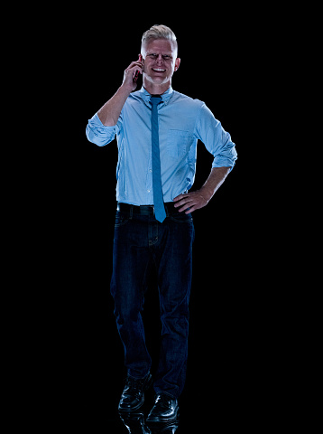 One person of aged 30-39 years old with short hair caucasian male business person standing in front of black background wearing pants who is talking and using smart phone