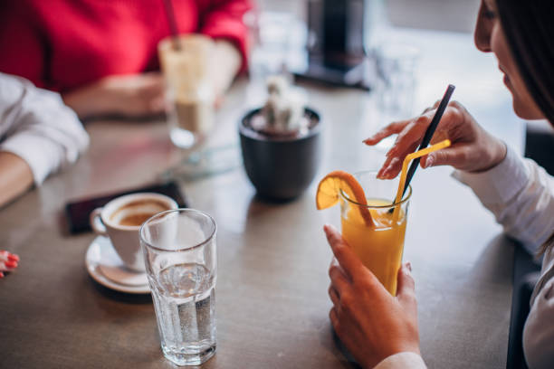 Close-up of a man's hands holding a cappuccino at a cafe, with a glass of orange juice and smartphone nearby