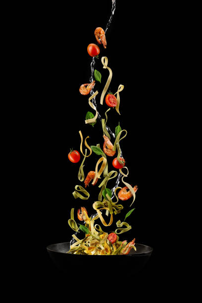 istock Wok pan, falling pasta with tomatoes, shrimps and green basil against black studio background. Poured by a water stream. Cooking concept. Close up 1239763904