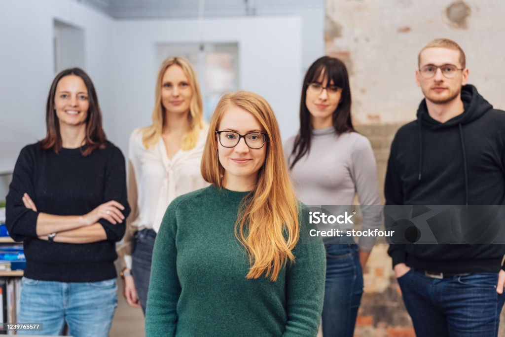 Young redhead woman with her business team Young redhead woman with her business team standing in the foreground smiling at the camera as they pose for a portrait Founder Stock Photo