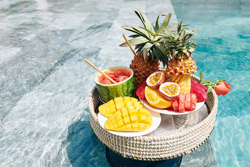 Various delicious exotic fruits on wicker tray floating in swimming pool
