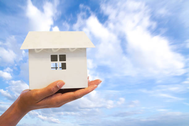 istock Close up Hand woman holding white house model isolate on blue sky background. Mortgage concept 1239771221