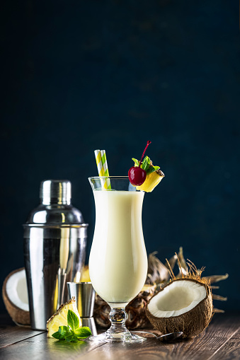 Glass of tasty Frozen Pina Colada Traditional Caribbean cocktail decorated by slice of pineapple and cherry, served on dark wooden background