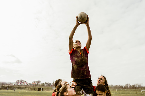 Photo of a female rugby player catching a ball, supported by her team