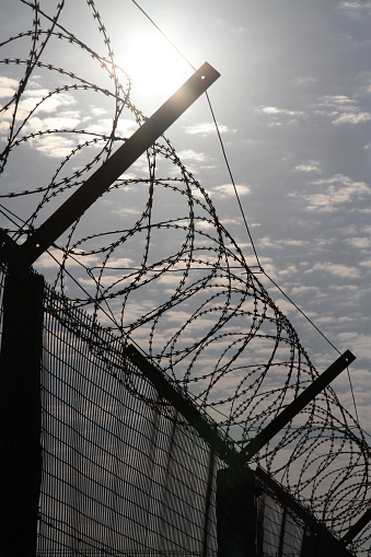 A silhouette of a Barbed Wire Prison Fence with a cloudy sky.