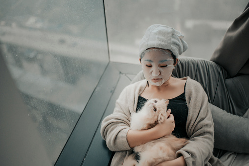 an asian chinese teenager girl  doing face spa mask with her cat in bedroom