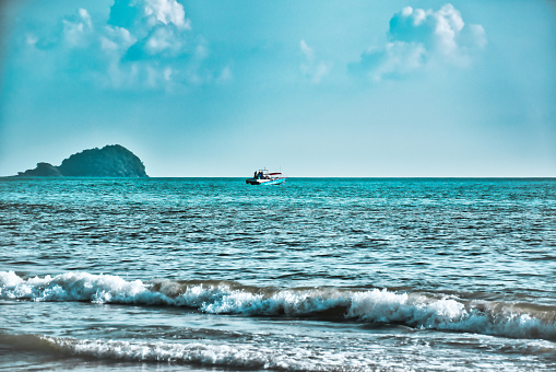Speed boat on the waves of the azure Andaman sea under the blue sky near the shores of the sandy beautiful exotic and stunning Cenang beach in Langkawi island, in Malaysia.