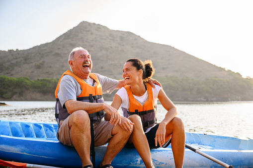 Affectionate and lighthearted senior male sitting on side of kayak with young female friend enjoying the pleasure of early morning exercise and good company.