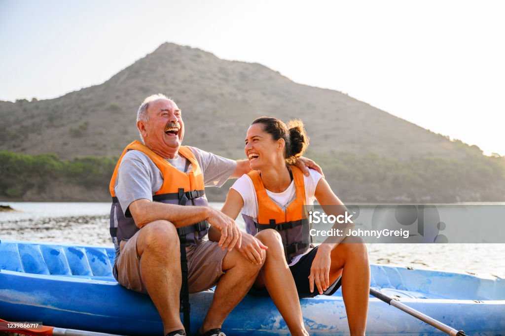 Spanish male and female enjoying early morning kayaking Affectionate and lighthearted senior male sitting on side of kayak with young female friend enjoying the pleasure of early morning exercise and good company. Senior Adult Stock Photo