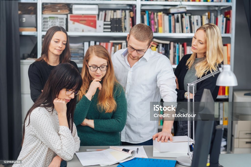 Business team reading through paperwork together Business team reading through paperwork together grouped around table with serious expressions in a book filled office Publisher Stock Photo