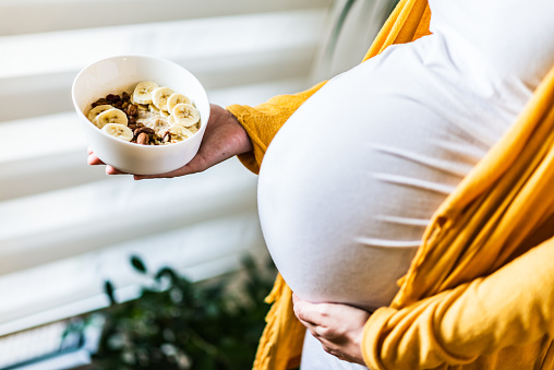 Pregnancy and healthy nutrition. Close-up of a pregnant woman's belly, holding oatmeal with bananas and hazelnut.