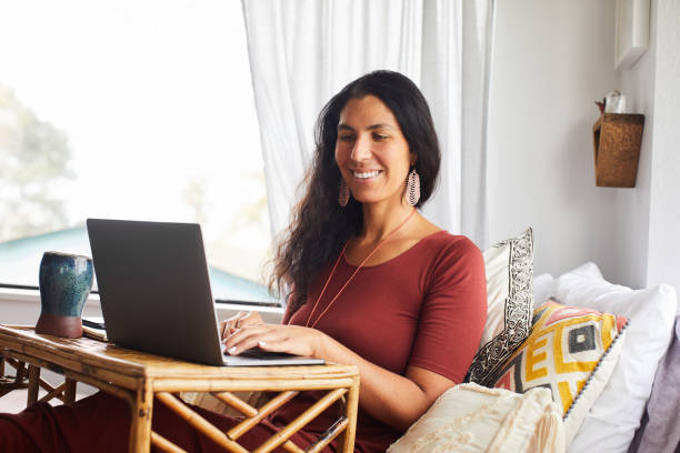 istock Smiling woman working on a laptop while sitting on her bed 1239943492
